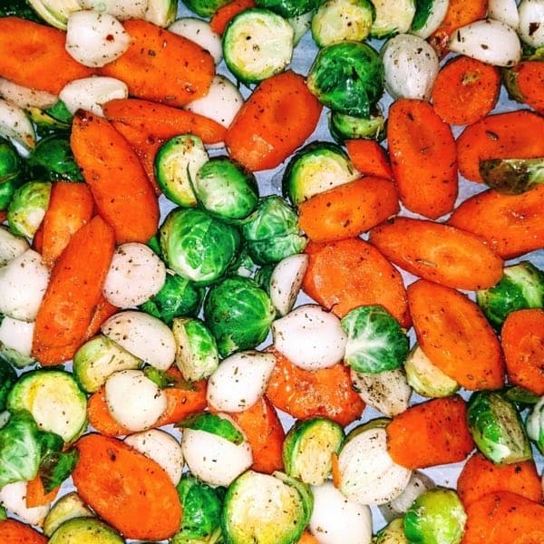 Sliced carrots, onion and halved Brussels sprouts spread out together, seen from above.