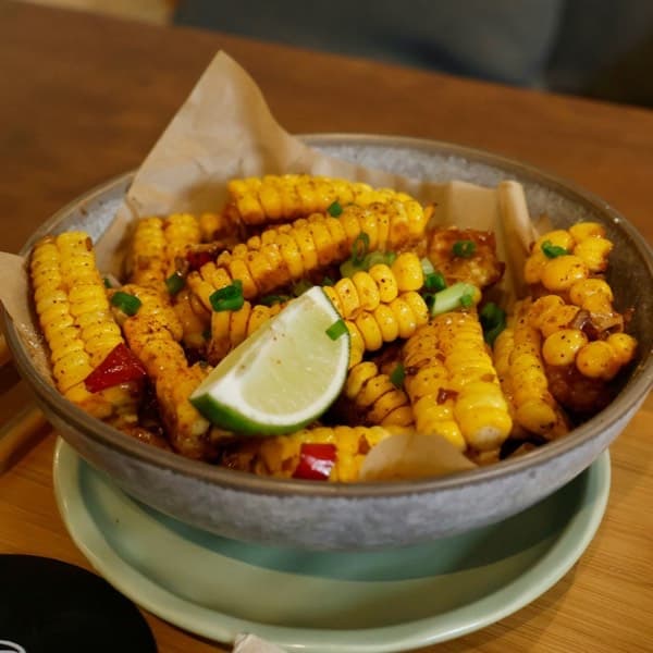 A bowl of seasoned corn on the cob pieces with a lime wedge on a wooden table.